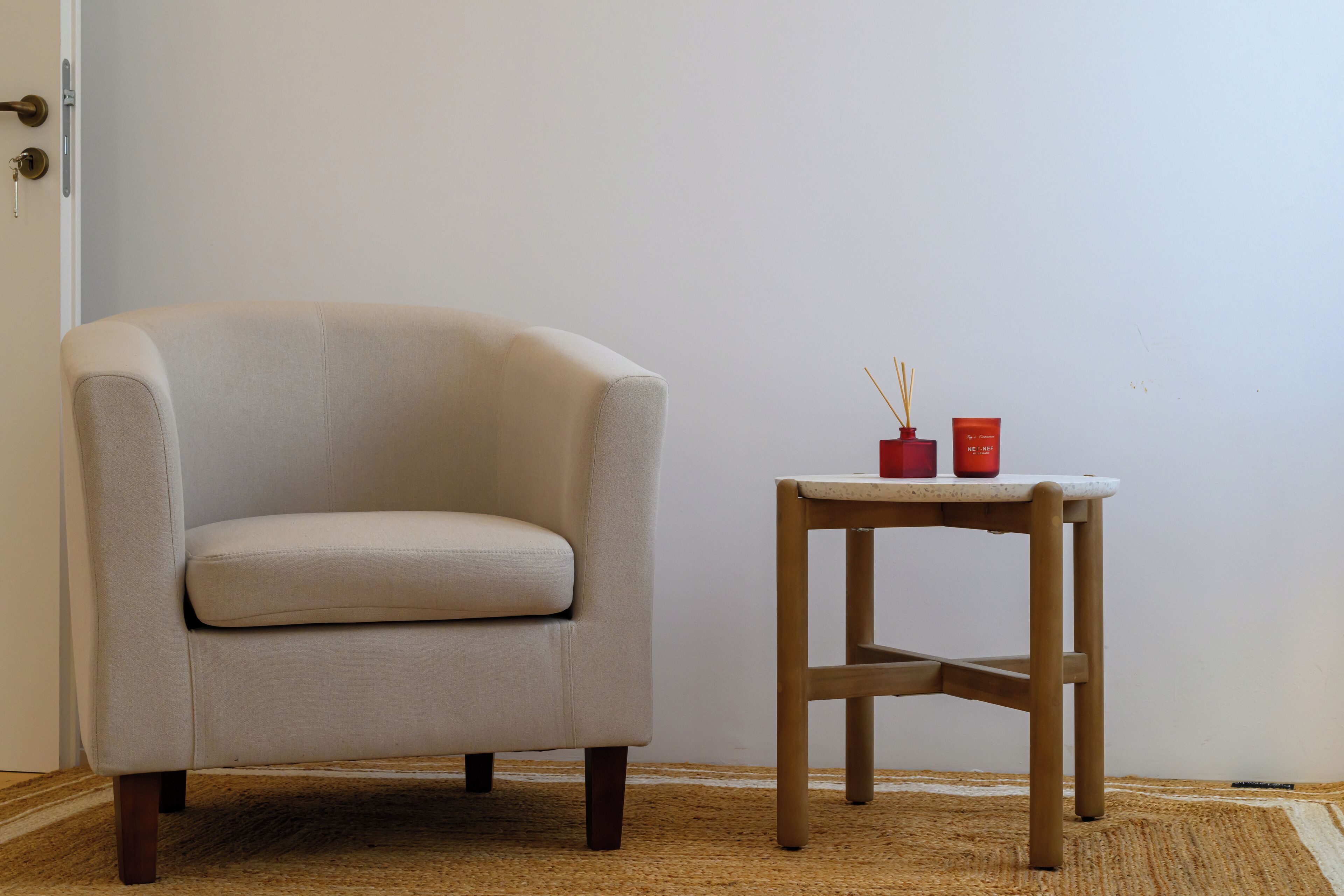 A beige armchair and a small wooden table with two red candle holders.