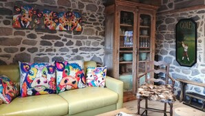 Ein gemütlicher Raum mit einer Steinwand, einem grünen Ledersofa mit bunten Kissen mit Tiermotiven, einer Holzkabine mit Glastüren und einem gerahmten Golfposter.