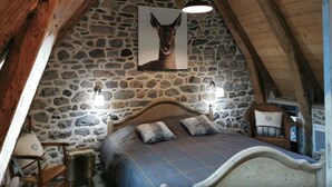 Ein gemütliches Schlafzimmer mit einer Steinwand, einem Bett mit blau-weiß karierter Bettdecke, zwei Nachttischlampen und einem gerahmten Bild von einem Hund an der Wand.