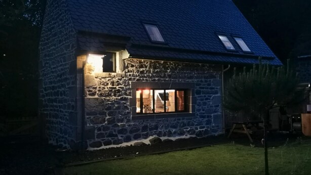 Ein Haus aus Stein mit geneigtem Dach, einem kleinen Fenster und einem beleuchteten Innenraum.