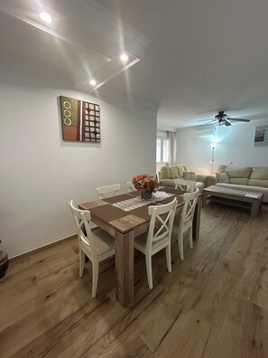 Ein Essbereich mit Holztisch und -stühlen, einem Deckenventilator und einer Couch im Hintergrund.