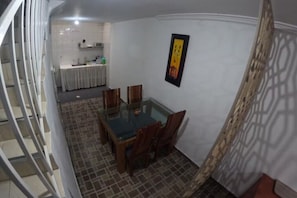 Ein Essbereich mit einem Glastisch und Holzsesseln, im Hintergrund eine Küche und eine Wand mit Muster.