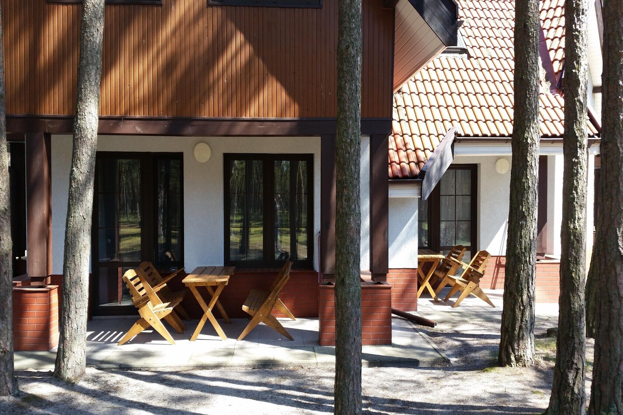 A wooden building with a covered patio area, outdoor seating, and a brick wall.