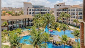 Een resort met een centraal gelegen zwembad, omgeven door palmbomen, meerduizendelingen en uitzicht op het omliggende landschap.