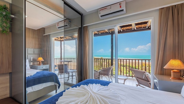 Een hotelkamer met balkon, een bed met wit- en blauwe dekbedovertrek, een nachtkastje met lamp en uitzicht op zee.
