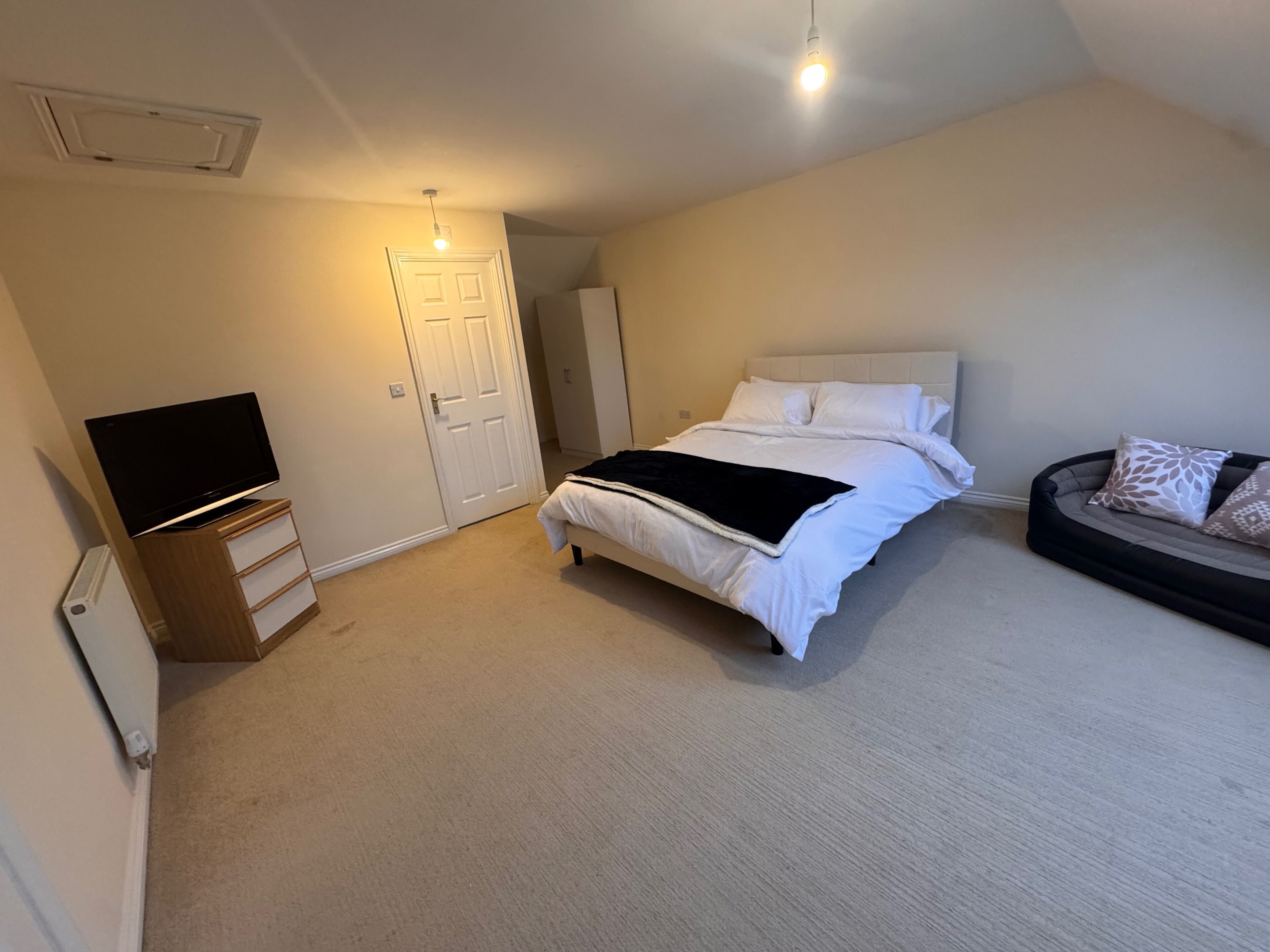 Ein Schlafzimmer mit einem Bett, einem Fernseher auf einem Schrank, einer Couch und einer Tür.