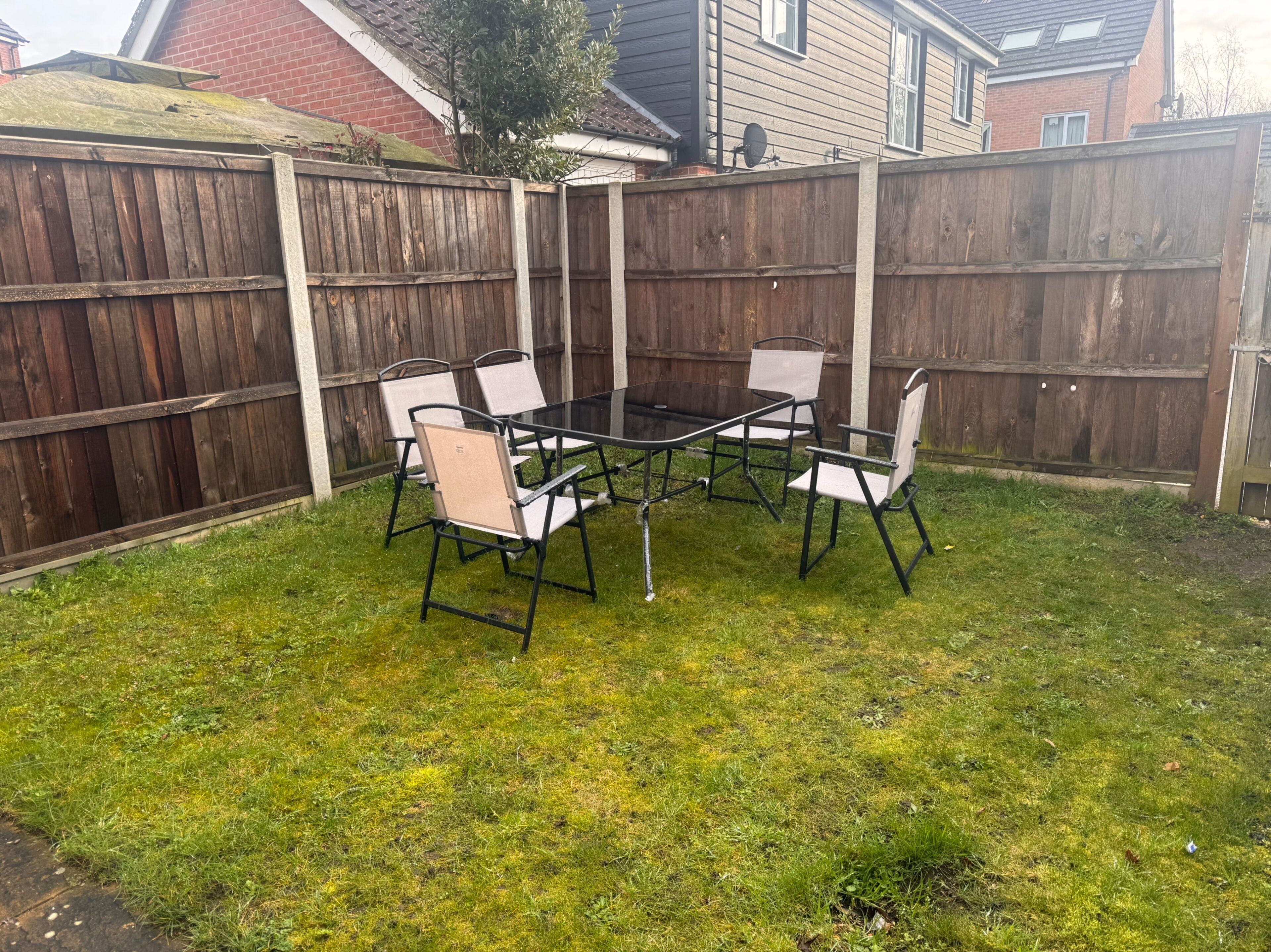 A backyard with a wooden fence, a glass table, and four chairs.