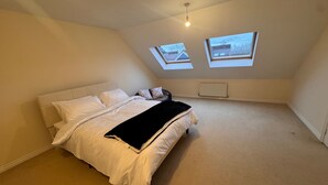 Ein Schlafzimmer mit einem Bett, zwei Oberlichtern, einer Heizung und einer Deckenleuchte.