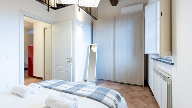 A bedroom with a bed, a wardrobe, a radiator, and a door leading to another room. - GuestHost - Cozy 50m2 attic apartment, ideal for 4 people, located on the first floor of a building without a lift (stairs to access it).The accommodation is located a stone's throw from the center of Lucca, a historic city that boasts symbolic places su (Lucca)