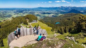 Um mirante cênico com uma plataforma de madeira, rodeado por florestas densas e uma vista panorâmica de um vale com montanhas ao longe.