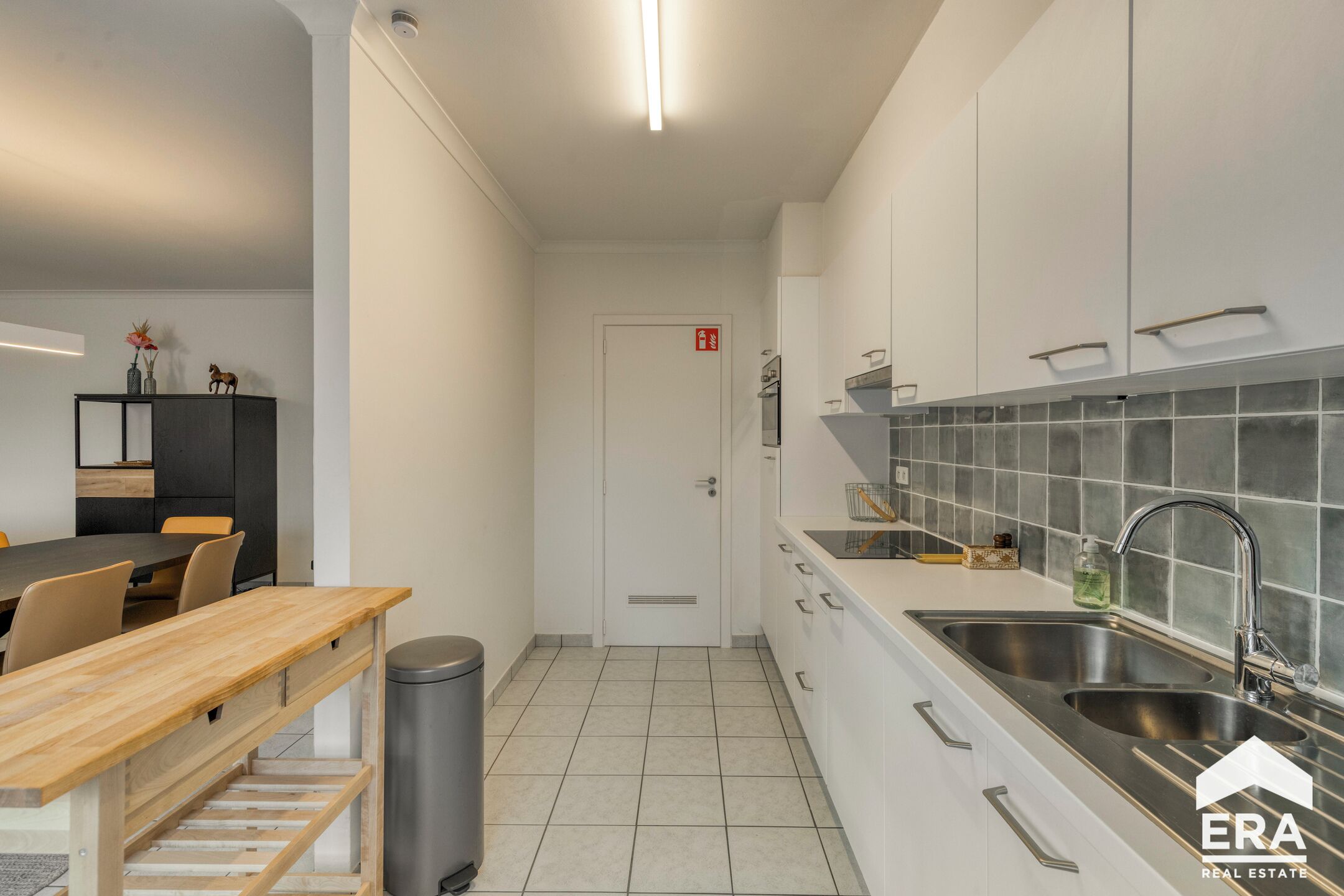A modern kitchen with white cabinets, stainless steel sinks, and a tiled backsplash.