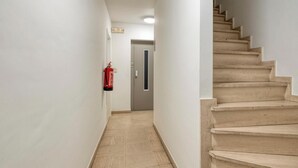 Un corridoio con un estintore a parete, una porta in fondo e una scala a destra.