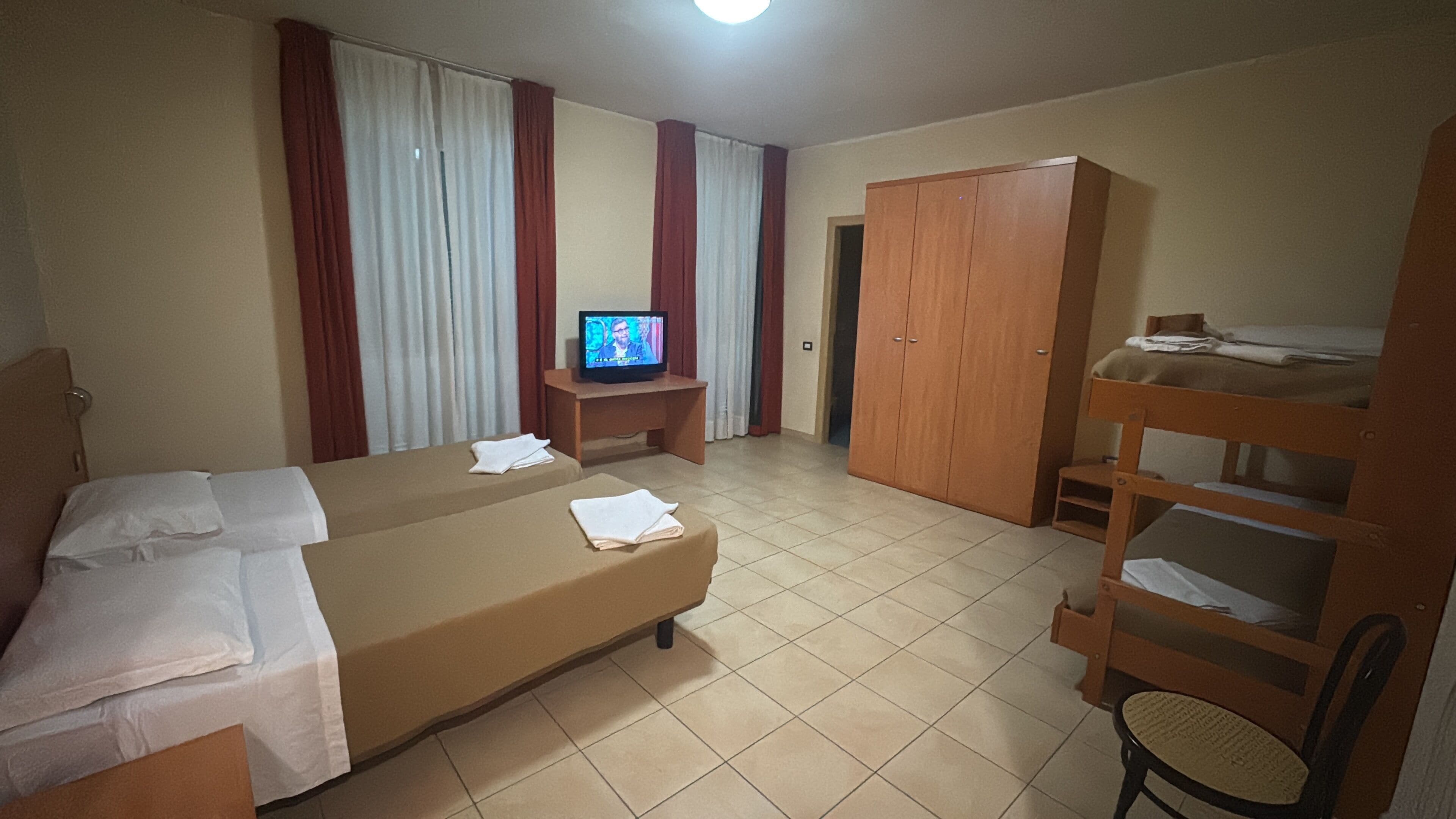 Habitación de hotel con dos camas, televisión, armario y litera.