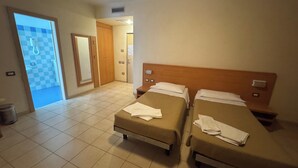 Ein Hotelzimmer mit zwei Betten, einem Badezimmer mit Schachbrettboden und einer sichtbaren Tür zu einem weiteren Zimmer.