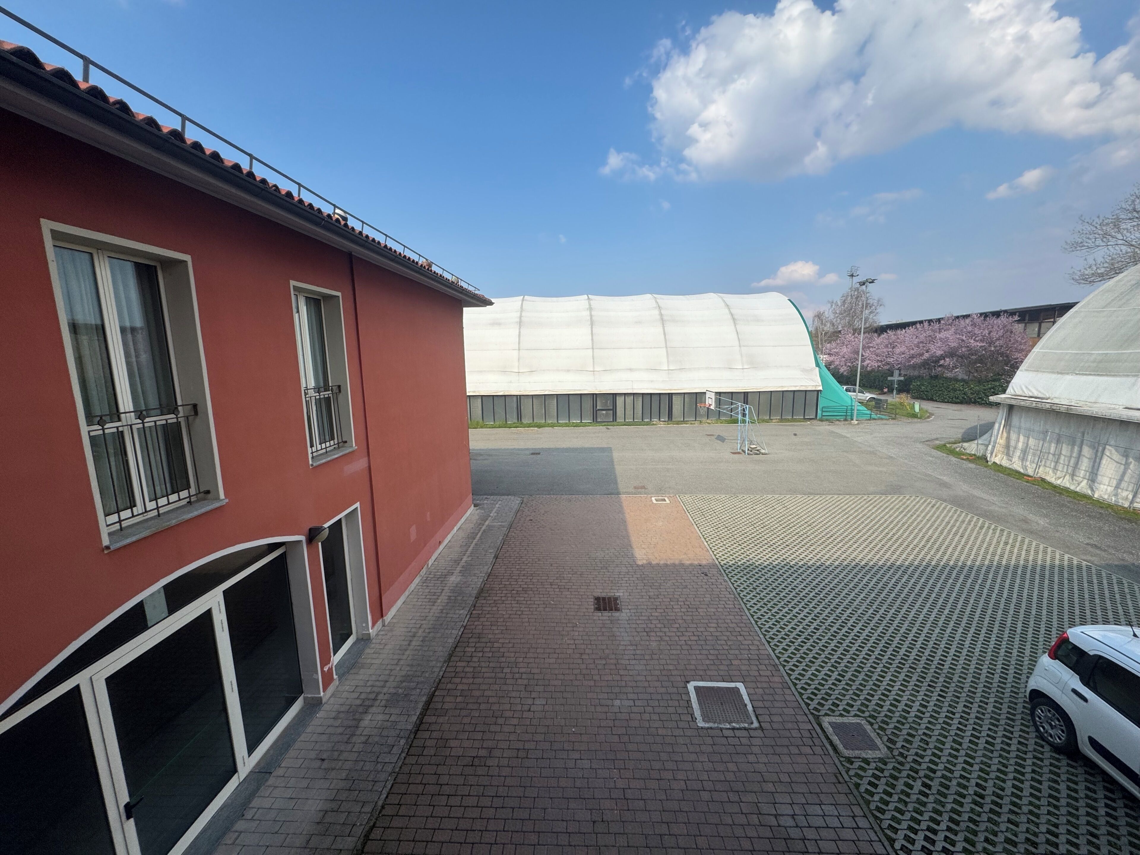 Un bâtiment rouge doté d’un espace extérieur couvert, d’un chemin pavé et d’une voiture garée.