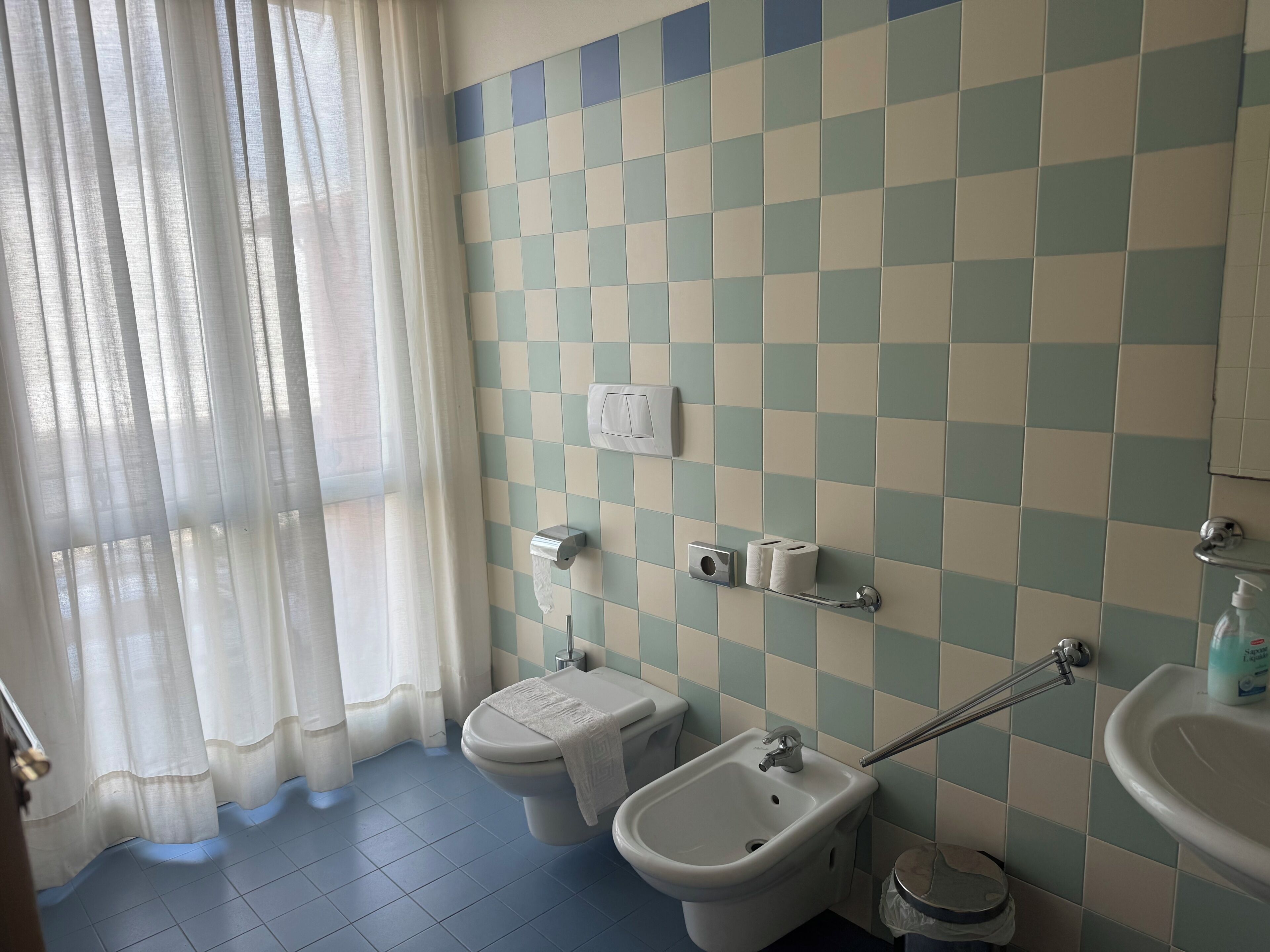 Une salle de bain avec un mur recouvert de carreaux à motifs, des toilettes, un bidet, un lavabo et un sèche-mains.