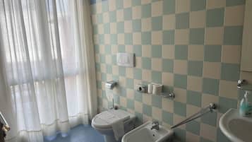 Bagno con parete rivestita di piastrelle a scacchiera, un water, un bidet, un lavandino e un asciugamani ad aria.