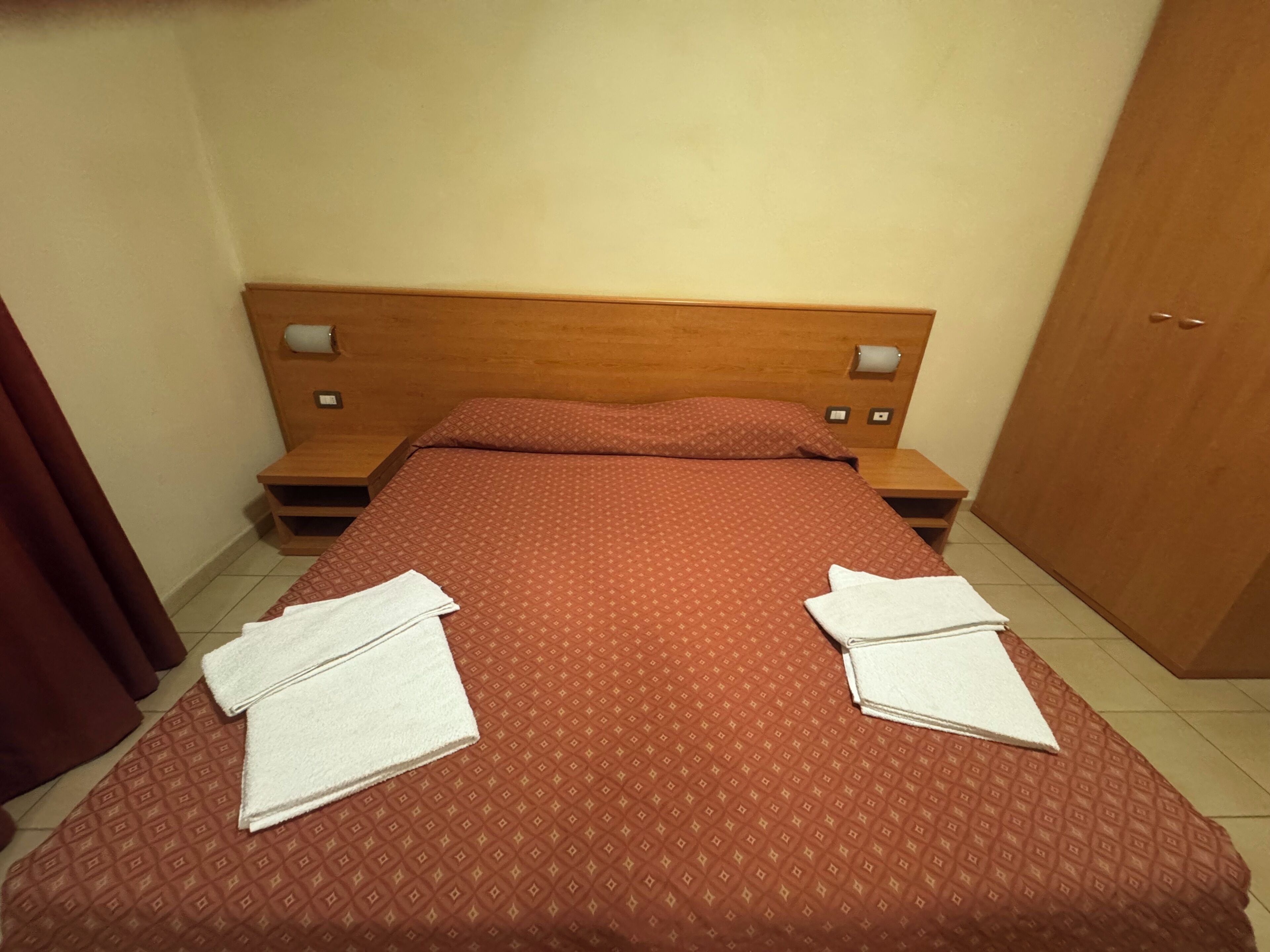 Una habitación de hotel con una cama, dos mesitas de noche, un cabecero de madera y un armario.
