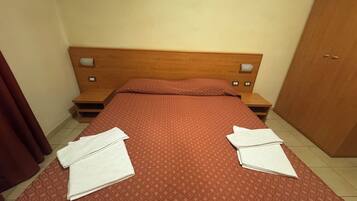 Una habitación de hotel con una cama, dos mesitas de noche, un cabecero de madera y un armario.