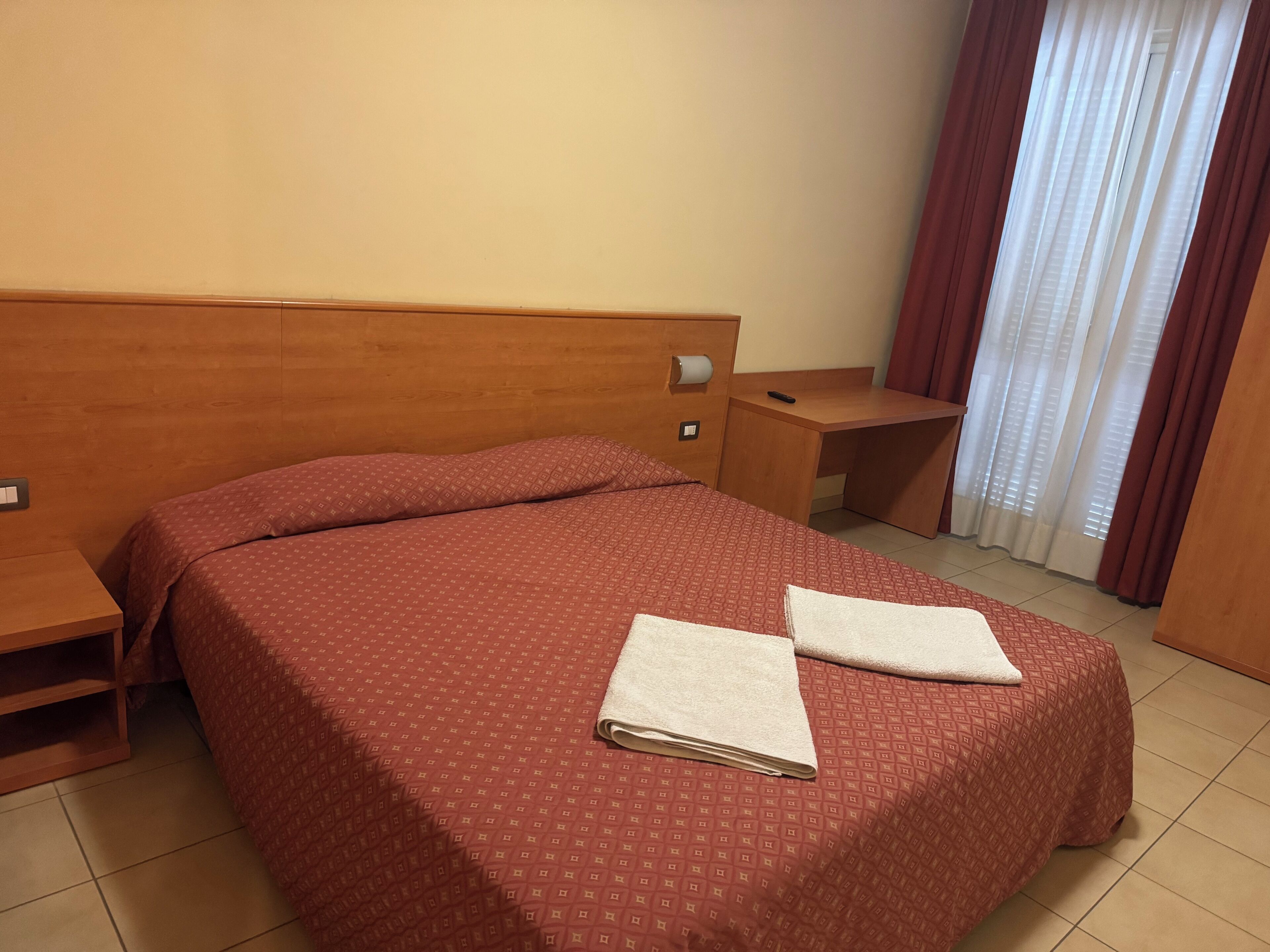 Una habitación de hotel con una cama grande, cabecera de madera, escritorio y ventana con cortinas.