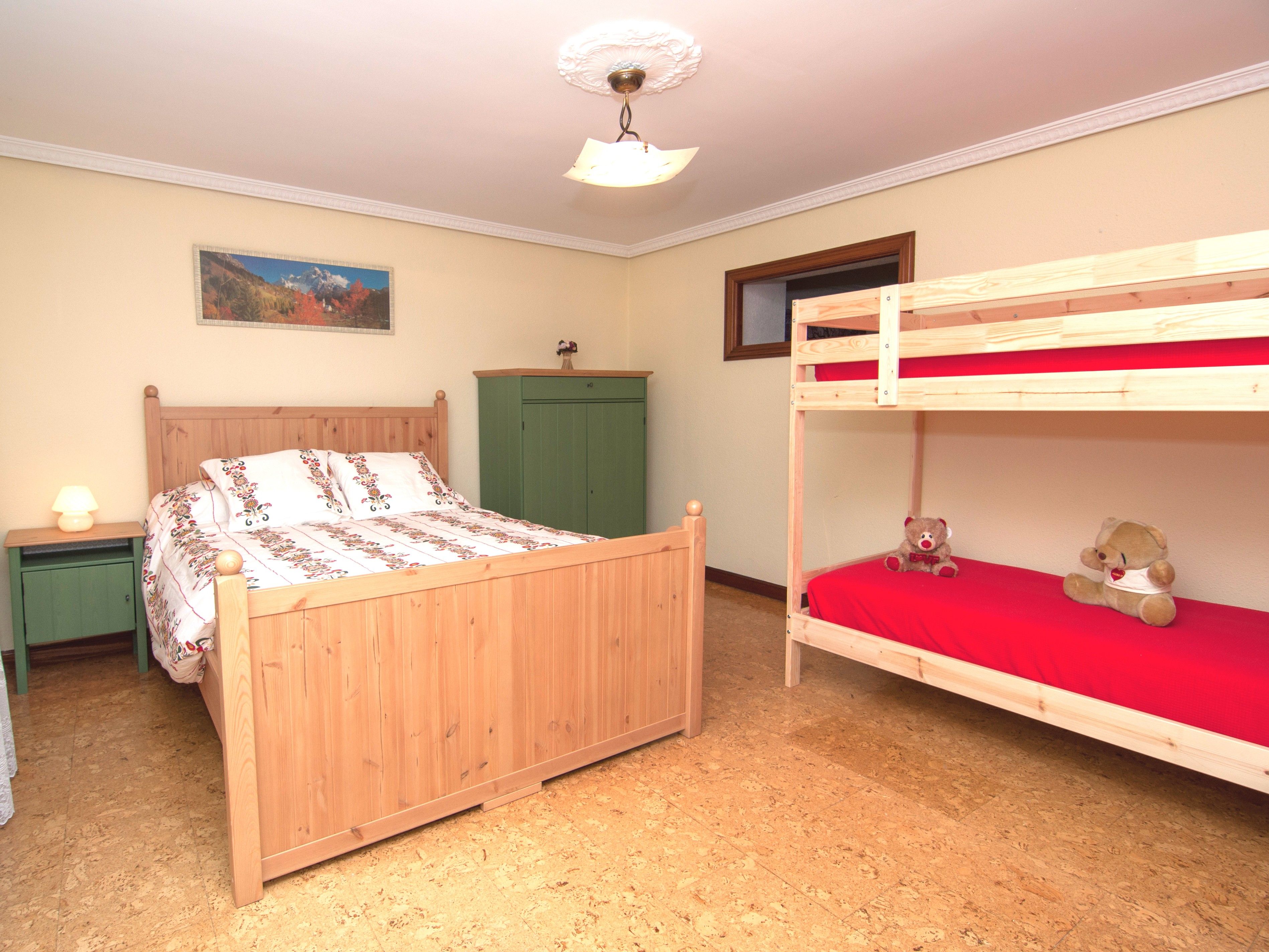 Una habitación con literas, un armario de madera, una mesita de noche con lámpara y un cuadro en la pared.