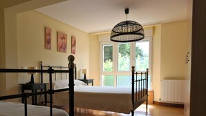 A bedroom with two beds, a window, a radiator, and artwork on the wall. - La Casona de Ilusión (Solórzano)