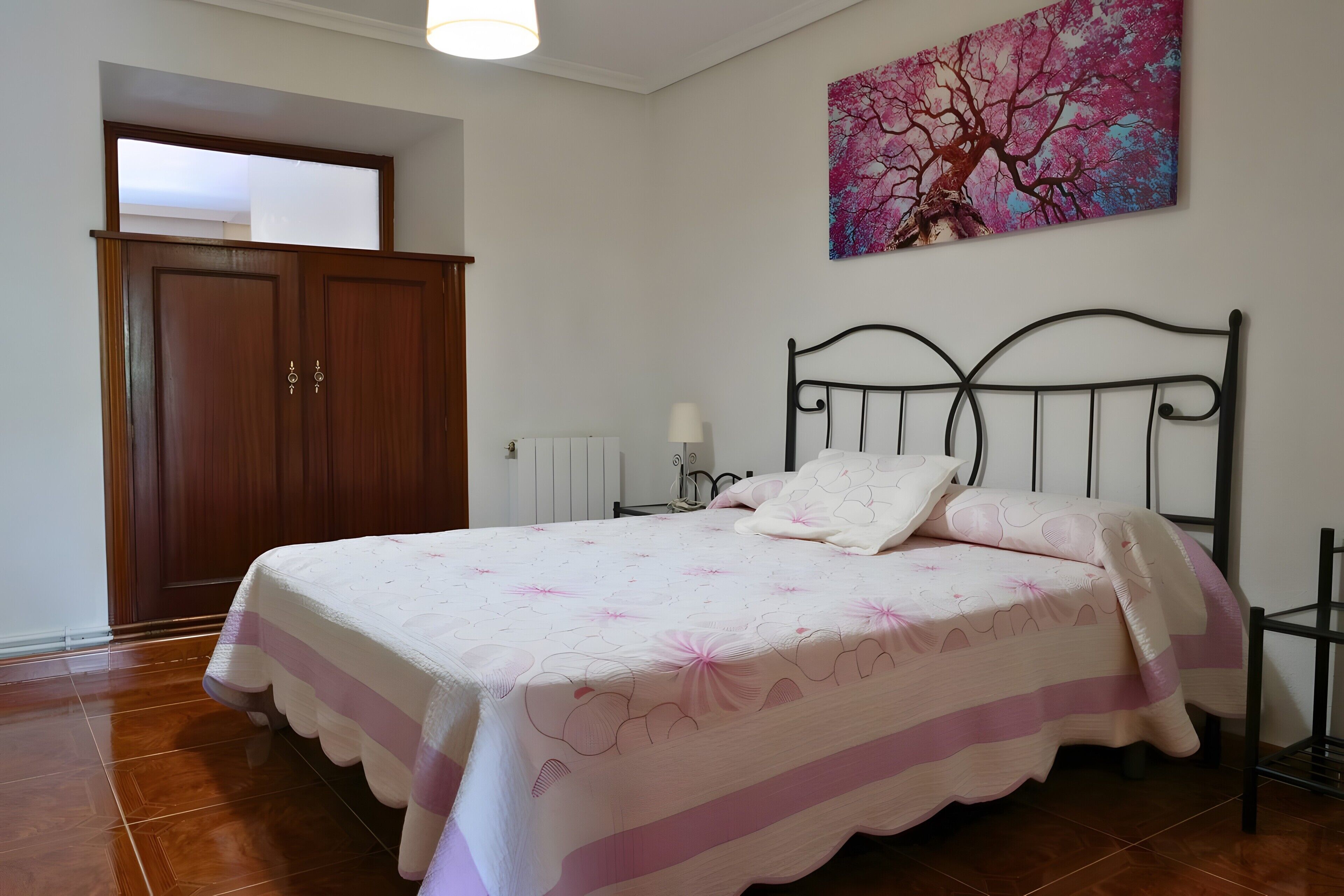 A bedroom with a bed, a wooden wardrobe, a radiator, and a painting on the wall.