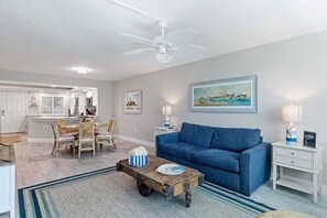 A modern living room with a blue sofa, a wooden coffee table, and a ceiling fan. - Your Perfect Beachfront Escape: Stunning Views & a Relaxing Screened Lanai (Sanibel)