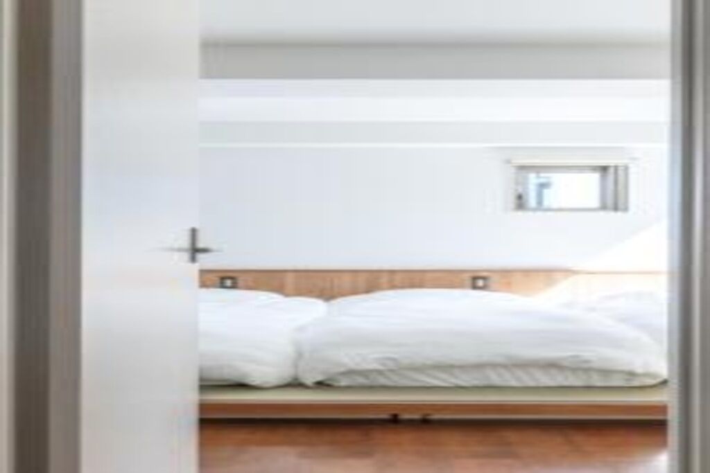A bedroom with a wooden bed frame, white bedding, and a small window.