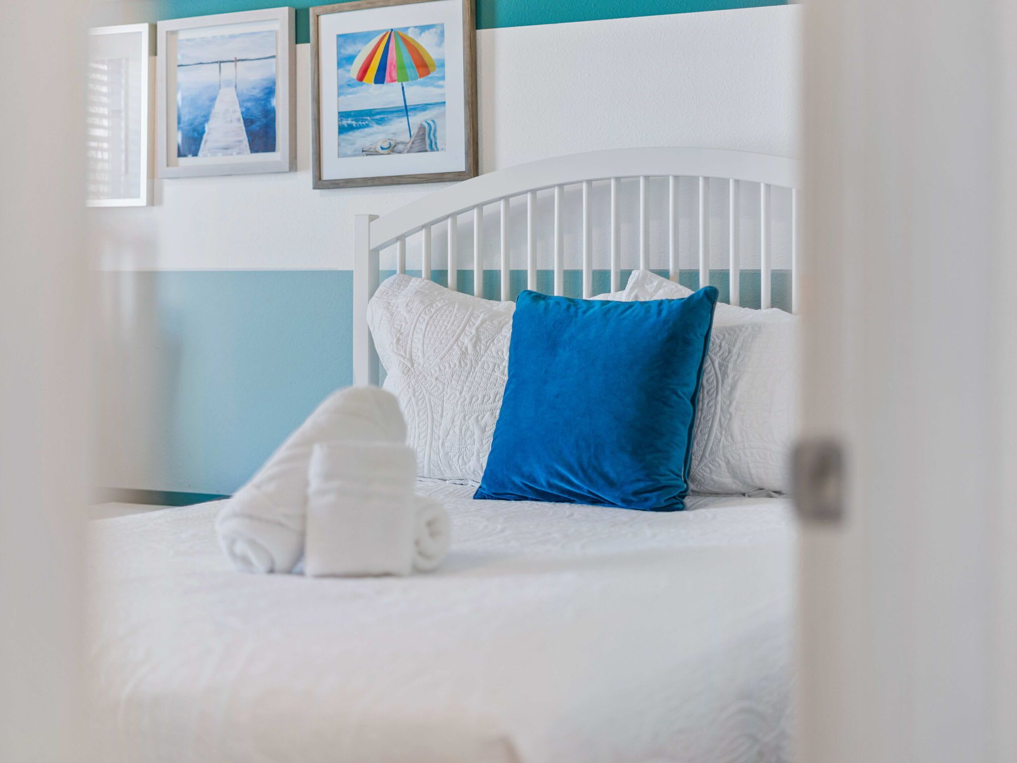 Uma cama bem arrumada com roupa de cama branca e azul, um painel de cabeceira branco e um travesseiro azul.