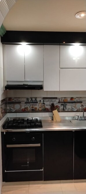 Una cuina moderna amb fogó a gas, forn i solera d'acer inoxidable. Hi ha armaris damunt el taulell i un frontal de mosaiques.