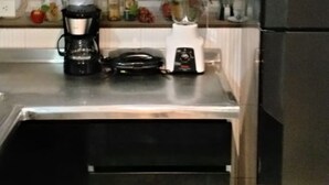 Una cocina con armarios blancos, un refrigerador negro, una cafetera y una licuadora en la encimera.