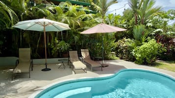 A swimming pool with lounge chairs and umbrellas, surrounded by lush greenery.