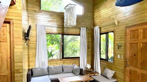 Interior de una cabaña de madera con un sofá, una mesita y una ventana con cortinas.