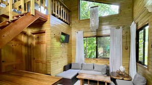 Interior de una cabaña de madera con sofá, mesa de comedor y una escalera.