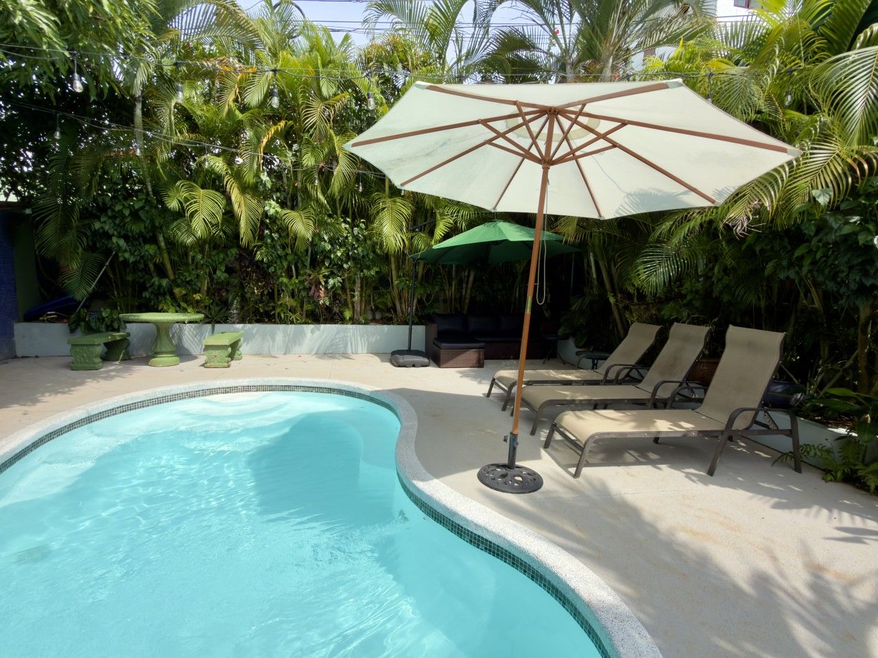 Una piscina con sillas de descanso y una mesa, rodeada de exuberante vegetación.