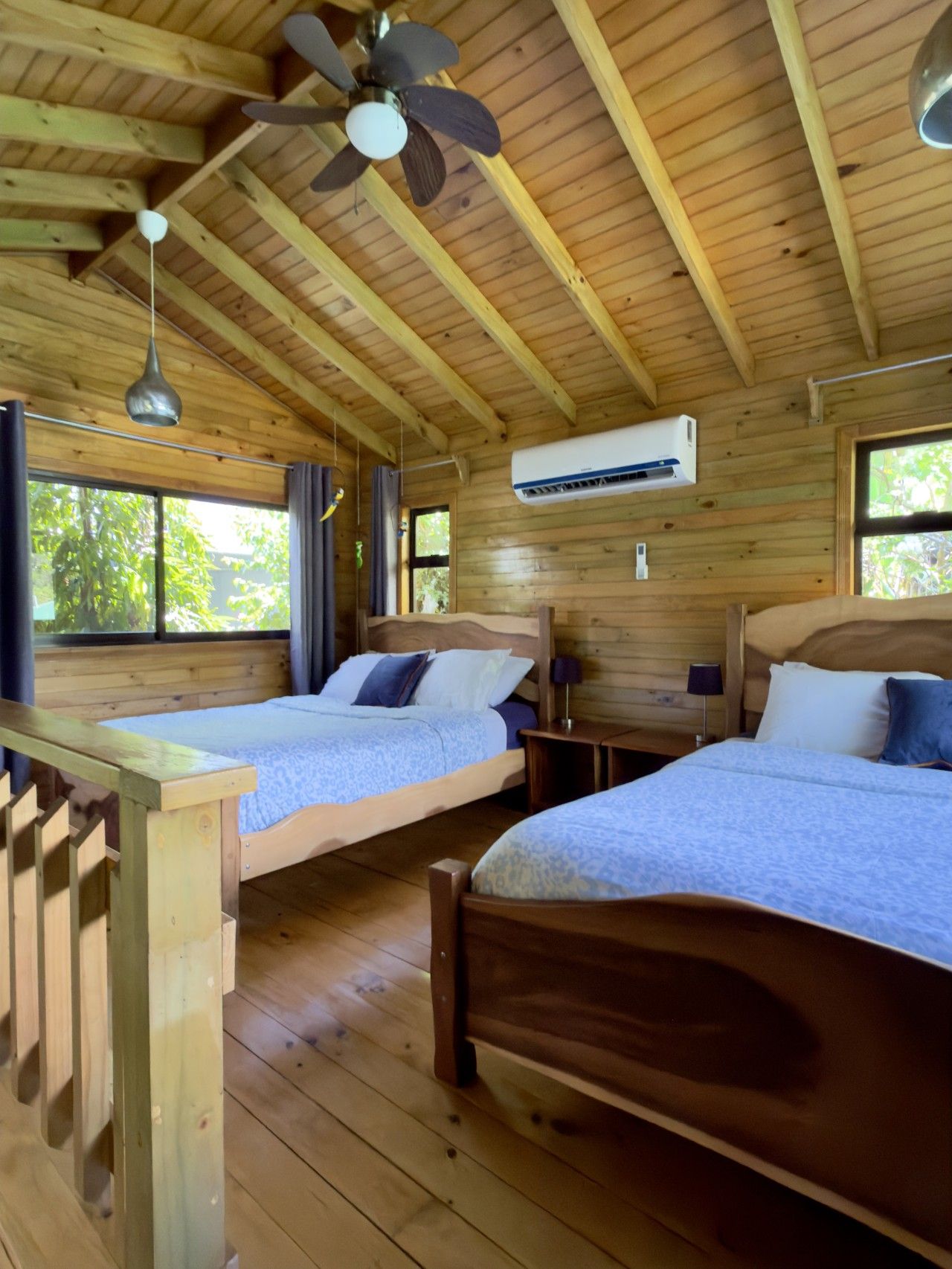 A cabin with two wooden beds, a ceiling fan, an air conditioning unit, and a window with curtains.