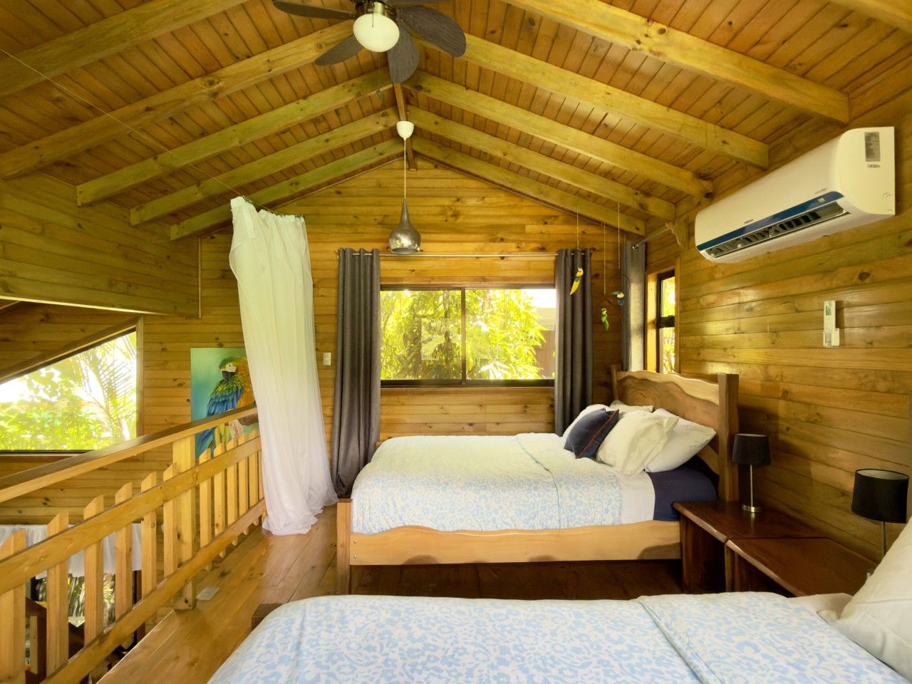 A wooden cabin bedroom with two beds, a ceiling fan, and a window with curtains.