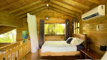 A wooden cabin bedroom with two beds, a ceiling fan, and a window with curtains.