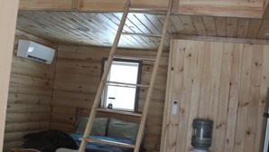 Eine Holzhütte mit Schlafzimmer im oberen Bereich, einer Leiter zum darüber liegenden Bett und einem kleinen Tisch sowie einem Wasserspender.
