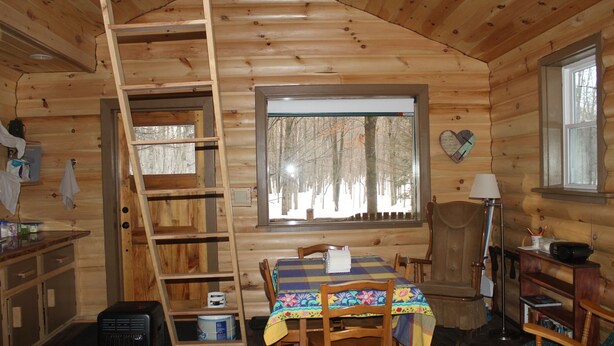 Ein Holzblockhaus-Interieur mit einem Esstisch, Stühlen, einer Leiter, einem Fenster und einer herzförmigen Dekoration an der Wand.