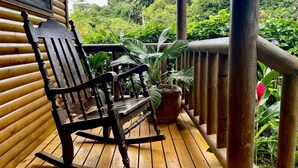 Una mecedora de madera sobre una terraza de madera, con una planta en maceta cerca.
