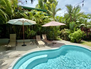 Une piscine entourée d’une végétation luxuriante, avec des chaises longues et des parasols.