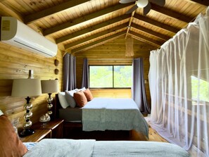 A cozy cabin room with a bed, a nightstand, a lamp, and a window with curtains. - Tropical Eco Cabin near Beach & Park (Manuel Antonio)