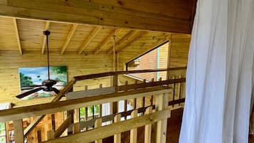 A wooden interior with a ceiling fan, a window, and a white curtain.