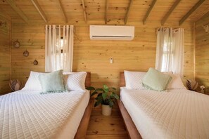 Habitación de cabaña de madera con dos camas, una planta en maceta y un equipo de aire acondicionado.