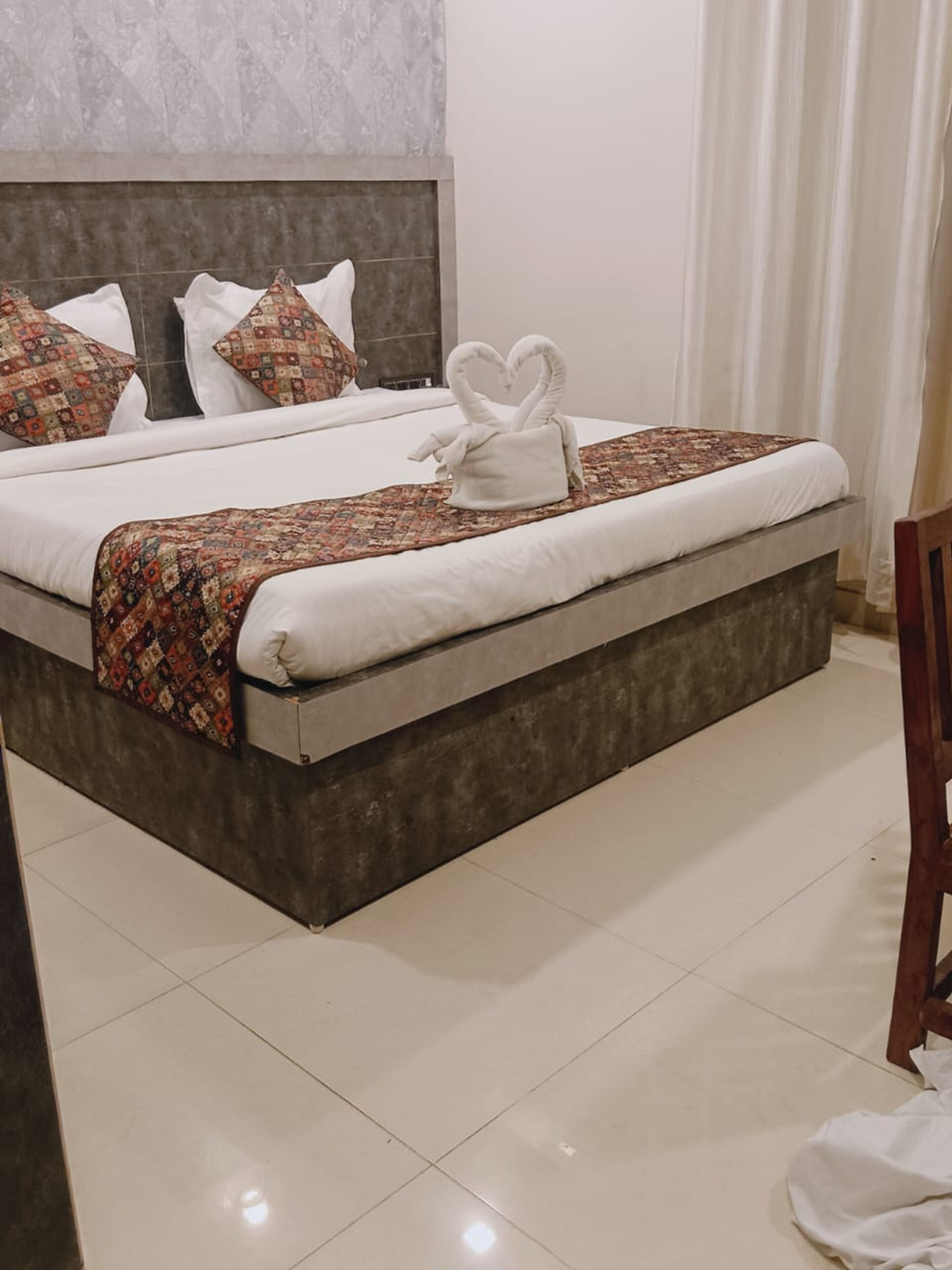 Une chambre d’hôtel avec un grand lit, une tête de lit, un plaid à motifs et une serviette en forme de cygnes posée sur le lit.