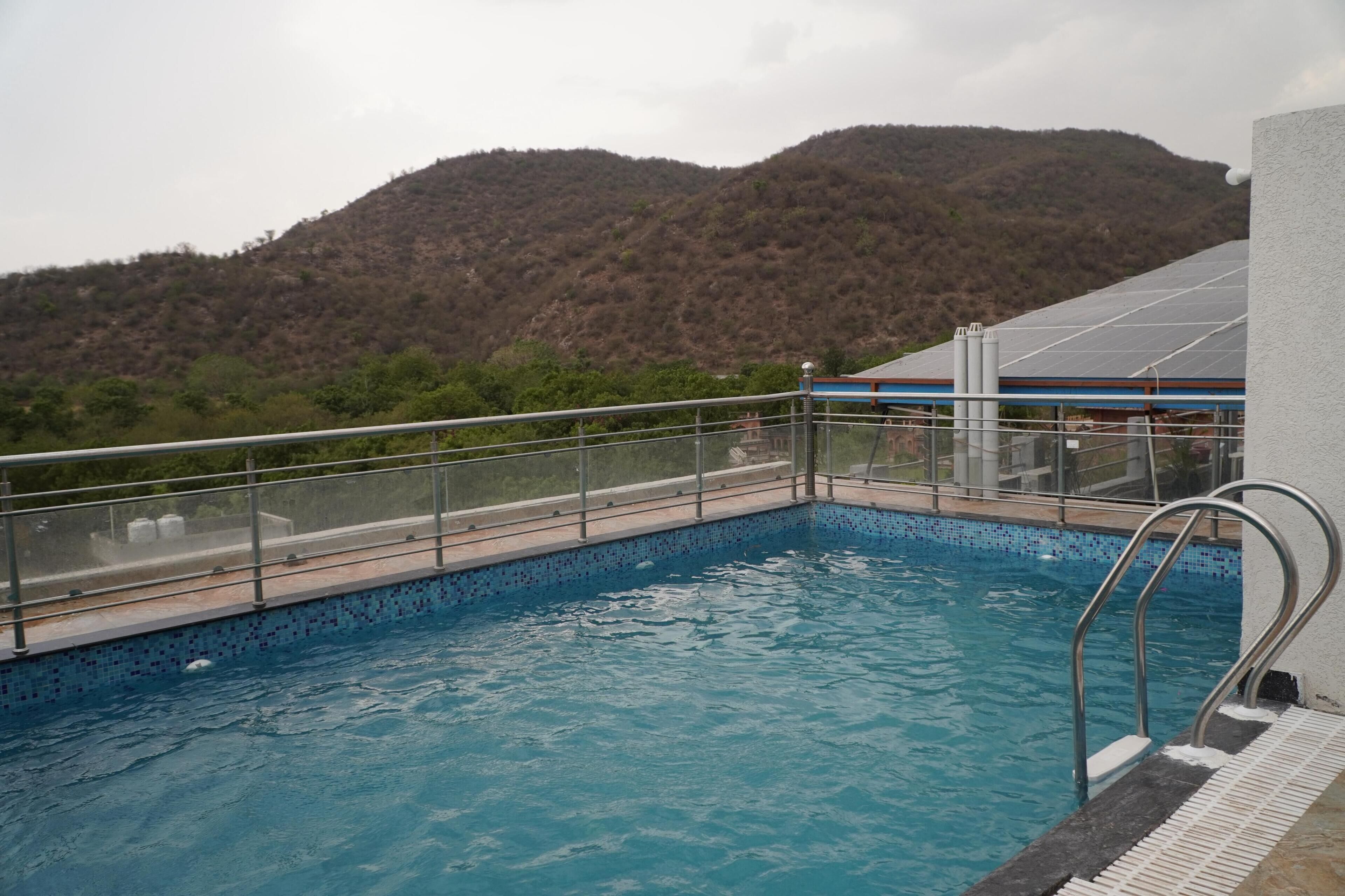 A swimming pool with a metal railing, surrounded by a mountainous landscape.