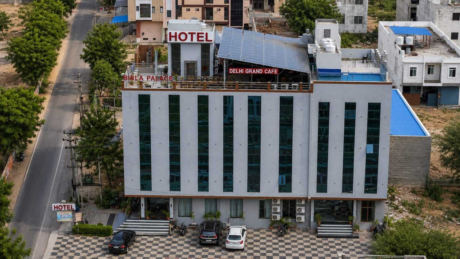 A hotel with a checkered entrance, a sign for 'BIRLA PALACE,' and a 'DELHI GRAND CAFE' on the roof.