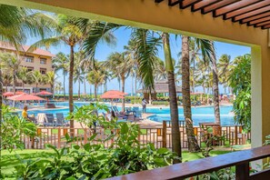 Zwembadgedeelte van een resort met palmbomen, ligbedden en parasols.